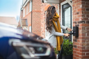 Women with yellow scarf charging blue electric vehicle.